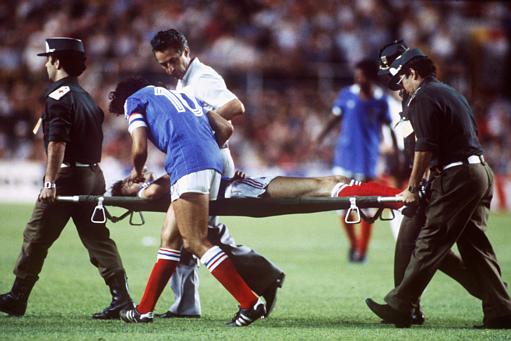 France's Patrick Battiston is carried off, escorted by captain Michel Platini.